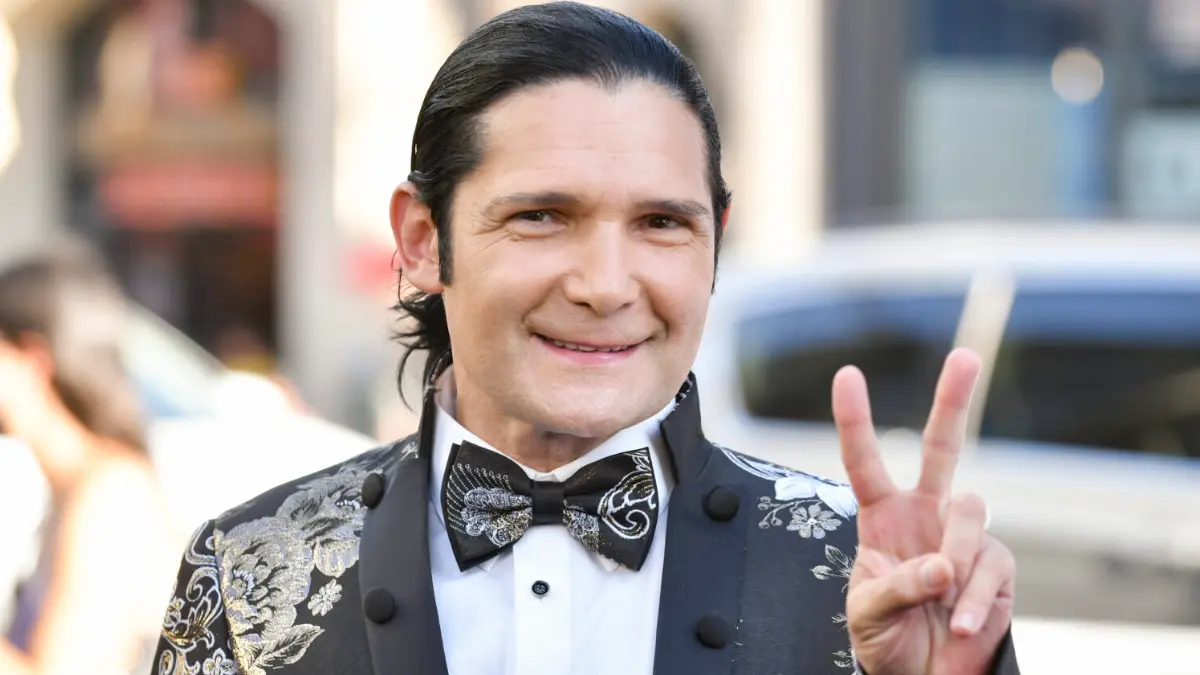 Corey Feldman Net Worth, Corey Feldman smiling and holding up a peace sign at a public event.