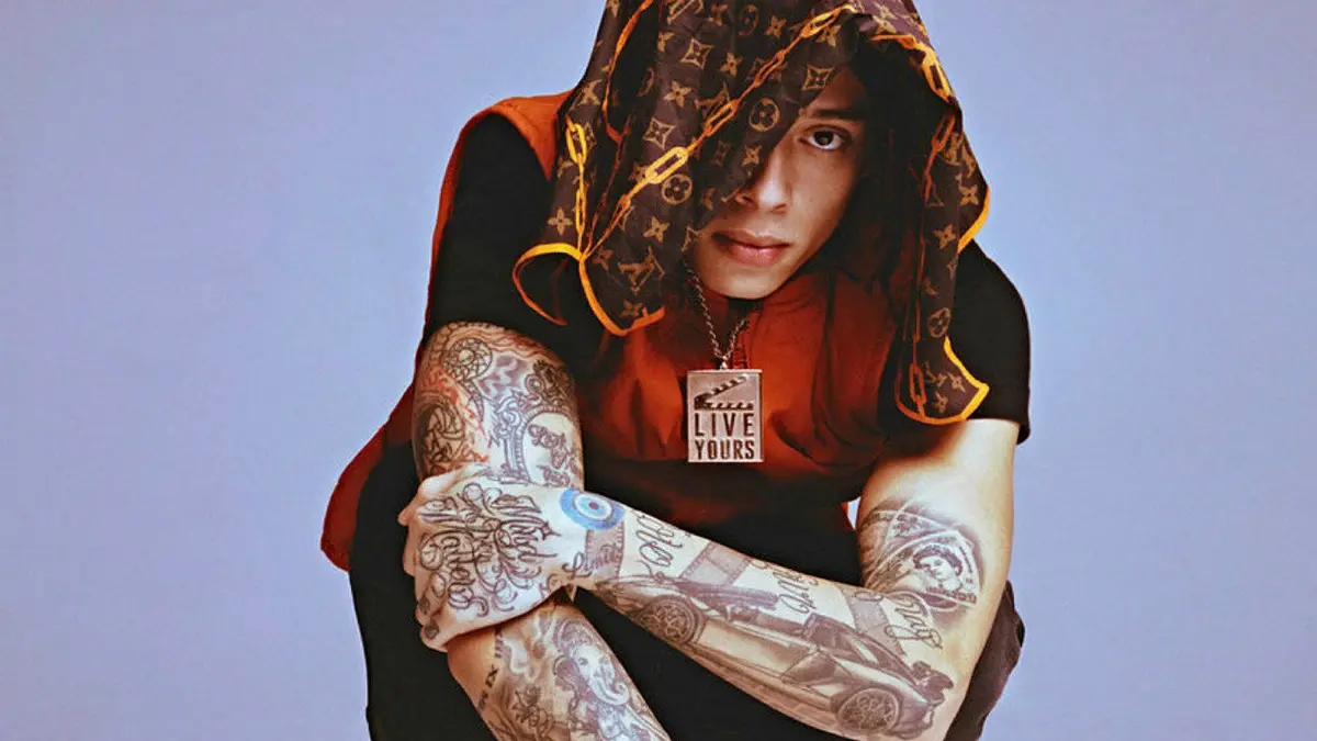 Central Cee wearing a hood and covering his face with a tattooed hand.